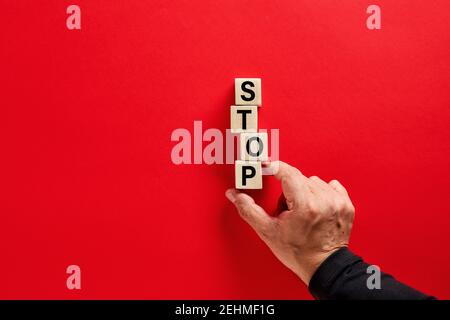 Männliche Hand die Holzblöcke mit dem Wort Stopp auf rotem Hintergrund mit Kopierraum anordnen. Entscheidung, das Konzept zu stoppen oder zu beenden. Stockfoto