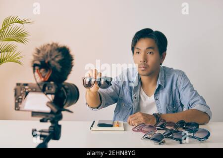 Asiatische Vlogger oder Blogger zeigen schwarze Mode-Brille mit Kunden vor der Kamera und Aufnahme von Video. Freelancer Online Live Streaming mit Custom Stockfoto