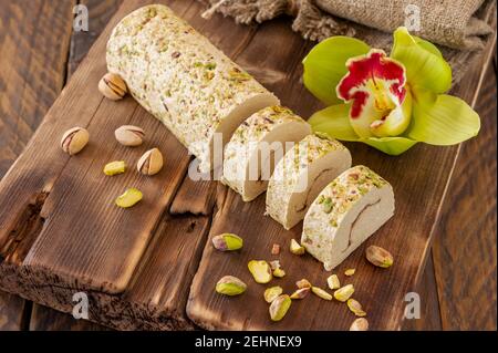 Tahini Halva in Scheiben mit Pistazie auf einem mit Blumen geschmückten Holzschreibtisch. Stockfoto