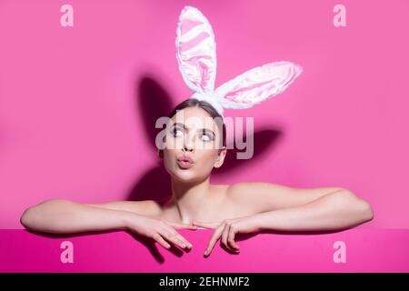 Ostern junge Frau Studio trägt Hasenohren. Neugierig isoliert auf rosa. Stockfoto