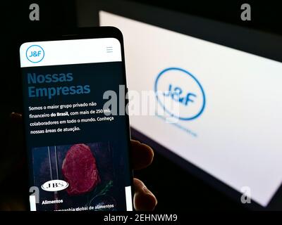 Person hält Handy mit Web-Seite der brasilianischen Investmentgesellschaft JF Investimentos SA auf dem Bildschirm mit Logo. Fokus auf der Mitte des Telefondisplays. Stockfoto