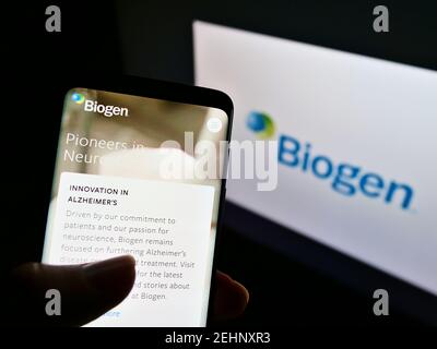 Person mit Mobiltelefon und Logo des US-Biotechnologieunternehmens Biogen Inc. Auf dem Bildschirm vor der Website. Fokus auf der Mitte des Handy-Displays. Stockfoto