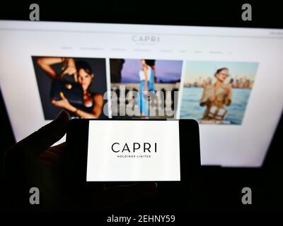 Person hält Smartphone mit Logo des Modeunternehmens Capri Holdings Limited auf dem Bildschirm vor der Website. Konzentrieren Sie sich auf die Telefonanzeige. Nicht modifiziertes Foto. Stockfoto