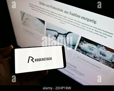 Person, die Mobiltelefon mit Firmenlogo des deutschen Brillenherstellers Rodenstock GmbH auf dem Bildschirm vor der Webseite hält. Konzentrieren Sie sich auf die Telefonanzeige. Stockfoto