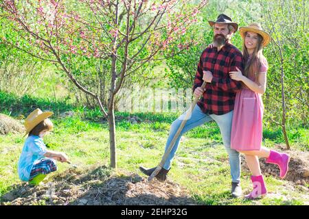 Familie Pflanze im Baumgarten im Frühjahr. Gruppenarbeit im frühlingshaften Hof mit Gärtnerwerkzeugen. Stockfoto