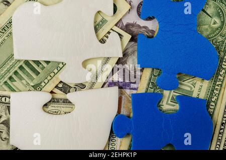Unter den Puzzleteilen sind amerikanische Dollar verschiedener Konfessionen versteckt. Blaue und weiße Rätsel. Draufsicht, Flat Lay. Stockfoto
