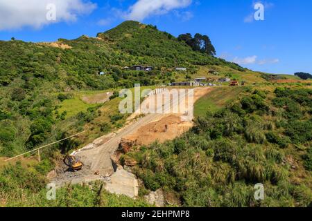 Straßenbau auf einem ländlichen Hügel in Neuseeland. Ein Bagger ist am Boden der Baustelle abgestellt Stockfoto