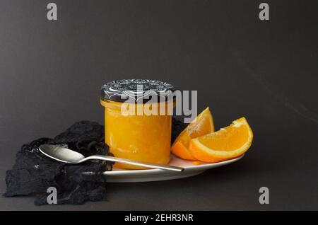 Orangenmarmelade in einem Glas auf einem Teller mit einem Löffel und Orangenscheiben Stockfoto
