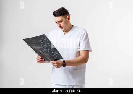 Junge männliche Arzt in weißen OP-Anzug halten und untersuchen Eine MRT-Untersuchung des Kopfes des Patienten, isoliert auf Weiß Hintergrund Stockfoto