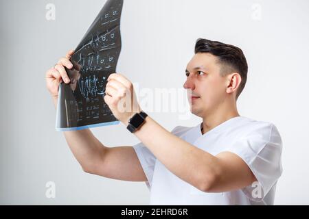 Junge männliche Arzt in weißen OP-Anzug halten und untersuchen Eine MRT-Untersuchung des Kopfes des Patienten, isoliert auf Weiß Hintergrund Stockfoto