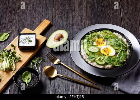 Quinoa Schüssel mit Ei, Sonnenblumen-Mikrogemüse, Gurke, Avocado, Baby Spinat in einer schwarzen Schüssel auf einem dunklen Holztisch, türkische Küche Stockfoto