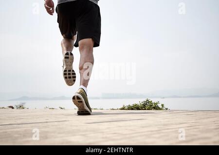 Nahaufnahme der Beine eines asiatischen Läufers, der am Meer läuft, Rückansicht
