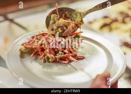 Mann legte etwas Schinken Gemüse und Mayonnaise Salat auf weißem Porzellanteller beim Essen Buffet, Nahaufnahme Detail Stockfoto