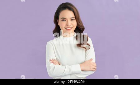 Foto von ernsthaften jungen Dame mit gekreuzten Armen in weißen Kleid gekleidet stehen und posieren über lila Hintergrund. Stockfoto