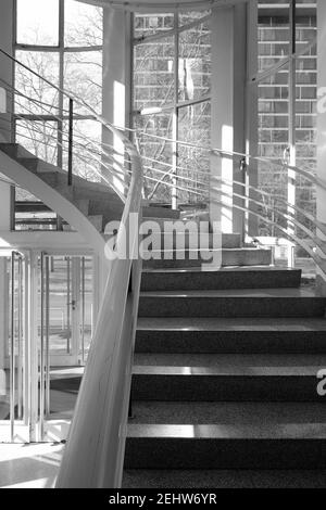 Graustufenaufnahme der modernen Wendeltreppe im Innenbereich mit Metallgeländer Stockfoto