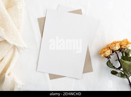 Modische Stock Schreibwaren Hintergrund - weiße Karte für Schriftzug und trockene gelbe Rosen auf einem weißen Tisch. Hochzeit femininer Hintergrund. Leer für ein in Stockfoto