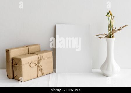 Leere weiße Grußkarte, Bastelschachteln und getrocknete Blumen in einer Vase auf weißem Hintergrund. Romantischer Hintergrund für die Einladung. Stockfoto