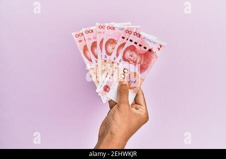 Hispanische Hand mit 100 chinesischen Yuan-Banknoten auf isoliertem rosa Hintergrund. Stockfoto