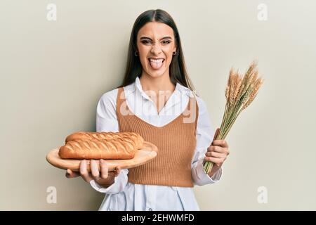 Schöne Brünette junge Frau hält hausgemachtes Brot und Spike Weizen ragt Zunge heraus glücklich mit lustigen Ausdruck. Stockfoto