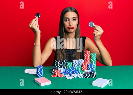 Junge hispanische Frau sitzt auf dem Tisch mit Casino-Chips deprimiert und sorgen für Not, Weinen wütend und Angst. Trauriger Ausdruck. Stockfoto