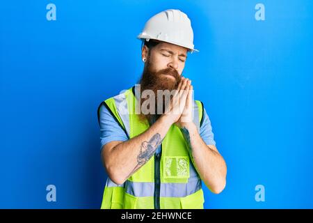 Rotschopf Mann mit langen Bart tragen Schutzhelm und reflektierend Jacke schlafen müde träumen und posieren mit den Händen zusammen, während Lächelnd mit clos Stockfoto