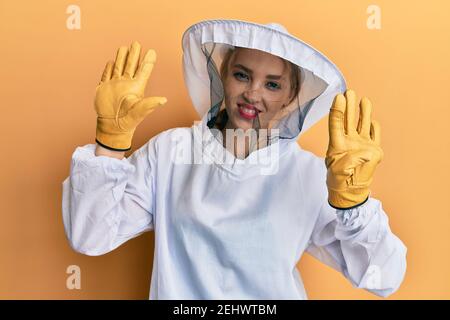 Schöne blonde kaukasische Frau trägt schützende Imker Uniform zeigen und Zeigt mit den Fingern Nummer neun nach oben und lächelt zuversichtlich und hap Stockfoto