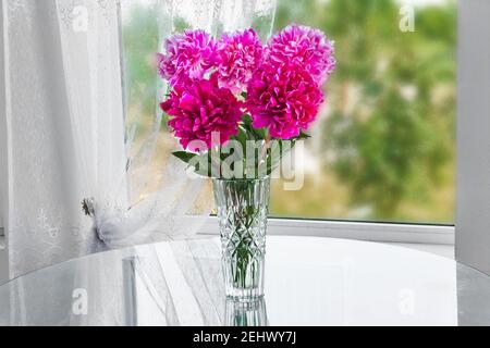 Ein Bouquet von fünf rosa Blumen Pfingstrosen stehen in der Zimmer auf dem Tisch in einer Kristallvase bei der Angezeigt Stockfoto