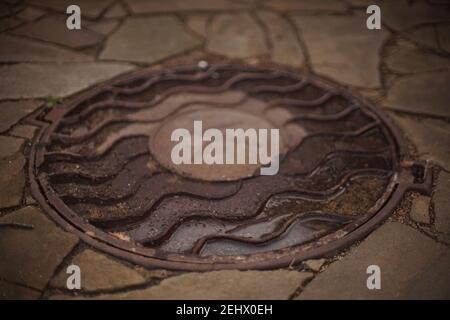 Altes Mannloch mit dem Buchstaben k und Pfützen nach dem Regen. Stockfoto