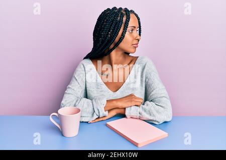 Schöne hispanische Frau, die ein Buch liest und einen Kaffee trinkt, der zur Seite schaut, relax Profil Pose mit natürlichem Gesicht mit selbstbewusstem Lächeln. Stockfoto