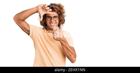 Junge hispanische Mann trägt Freizeitkleidung und Brille lächelnd machen Rahmen mit Händen und Fingern mit glücklichen Gesicht. Kreativität und Fotografie Konzept. Stockfoto