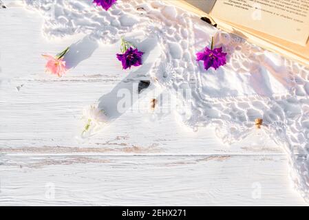 Violette Blumen auf einem Buch. Durchbrochene gestrickte Tischdecke auf einem alten Holztisch. Abend im Dorf. Sonnenuntergang im Freien, Batanica, schöne Blumen Stockfoto