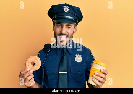 Handsome hispanischen Polizei Mann essen Donut und trinken Kaffee Kleben Zunge aus glücklich mit lustigen Ausdruck. Stockfoto