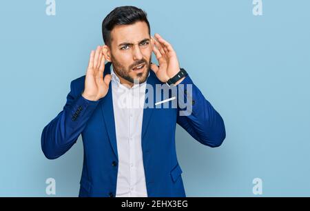Junge hispanic Mann trägt Business Jacke versucht, beide Hände auf Ohr Geste hören, neugierig auf Klatsch. Hörproblem, taub Stockfoto