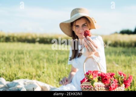 Feld in Gänseblümchen, ein Blumenstrauß.Französisch Stil romantische Picknick-Einstellung. Frau in Baumwollkleid und Hut, Erdbeeren, Croissants, Blumen auf Stockfoto