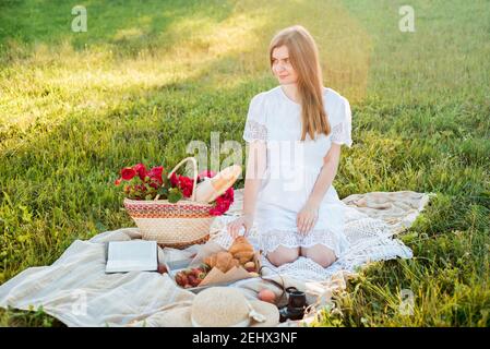 Feld in Gänseblümchen, ein Blumenstrauß.Französisch Stil romantische Picknick-Einstellung. Frau in Baumwollkleid und Hut, Erdbeeren, Croissants, Blumen auf Stockfoto