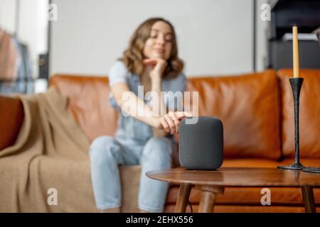 Frau berührt schwarzen Audio-Assistent Spalte auf dem Couchtisch Stockfoto