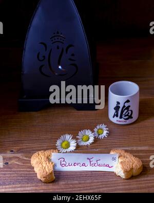Ein Keks in der Hälfte mit dem italienischen Satz, die gespalten Bedeutet Glück und eine Tasse mit dem japanischen Wort Glück auf einem dunklen Hintergrund Stockfoto