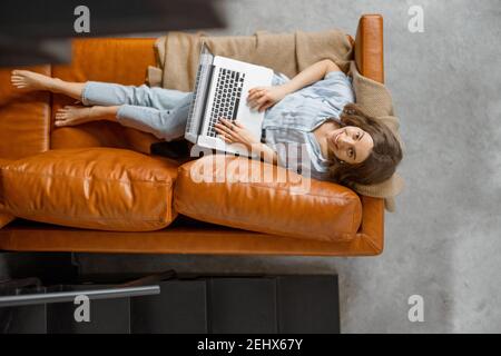 Frau, die von zu Hause aus mit einem Laptop auf dem Sofa arbeitet Stockfoto
