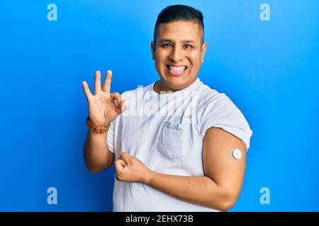 Junge lateinische Mann mit Glucose-Meter-Taste tun ok Zeichen mit Fingern, lächelnd freundlich gestikulieren ausgezeichnete Symbol Stockfoto