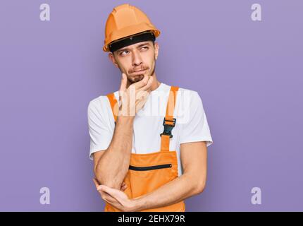 Hispanic junger Mann trägt Handyman Uniform und Sicherheit Hardhut ernstes Gesicht Denken über Frage mit Hand auf Kinn, nachdenklich über verwirrende Idee Stockfoto