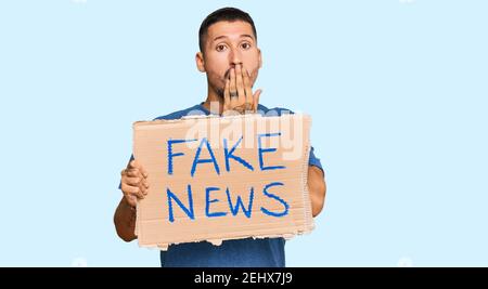 Schöner Mann mit Tätowierungen hält gefälschte News-Banner über den Mund mit der Hand, schockiert und Angst vor Fehler. Überrascht Ausdruck Stockfoto