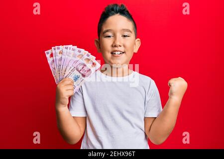 Kleiner Junge hispanic Kind hält 50 mexikanische Pesos Banknoten schreien stolz, feiert Sieg und Erfolg sehr aufgeregt mit erhobenem Arm Stockfoto