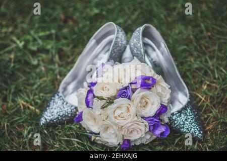 Schuhe der Braut mit einem Brautstrauß auf dem grünen Gras. Nahaufnahme. Stockfoto