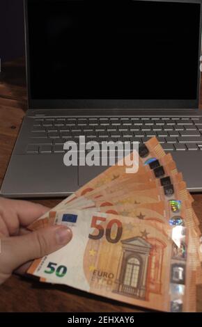 Geld vor einem Laptop auf einem Holztisch Stockfoto