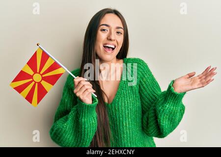 Junge hispanische Mädchen hält mazedonische Flagge feiert Leistung mit glücklich Lächeln und Sieger Ausdruck mit erhobener Hand Stockfoto