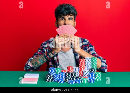 Junge hispanic Mann spielen Glücksspiel Poker Abdeckung Gesicht mit Karten ragen Zunge aus glücklich mit lustigen Ausdruck. Stockfoto