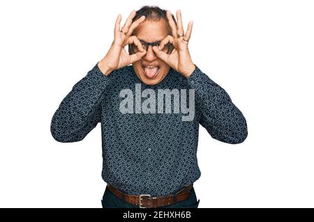 Mittelalter indischer Mann trägt lässige Kleidung und Brille tun ok Geste wie Fernglas aufragende Zunge aus, Augen durch die Finger schauen. Verrückte exp Stockfoto