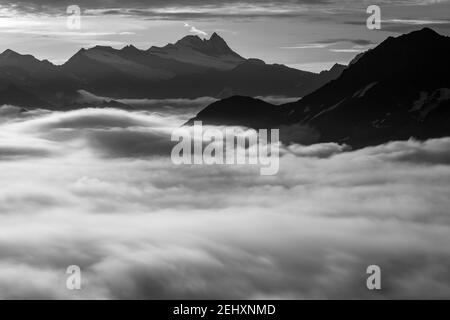 Blick auf die Westseite der Glockner-Gruppe. Großglockner Berggipfel. Sich bewegende Wolken. Österreichische Alpen. Europa. Schwarz-weiße Landschaft. Stockfoto