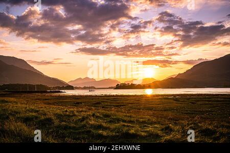 Sonnenuntergang am Loch Leven, Glencoe, Schottland. Farbenprächtiger Sonnenuntergang am Loch Leven mit einem Boot und einer Silhouette der Fort William Bridge am Horizont. Stockfoto