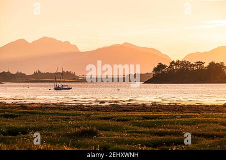 Sonnenuntergang am Loch Leven, Glencoe, Schottland. Farbenprächtiger Sonnenuntergang am Loch Leven mit einem Boot und einer Silhouette der Fort William Bridge am Horizont. Stockfoto